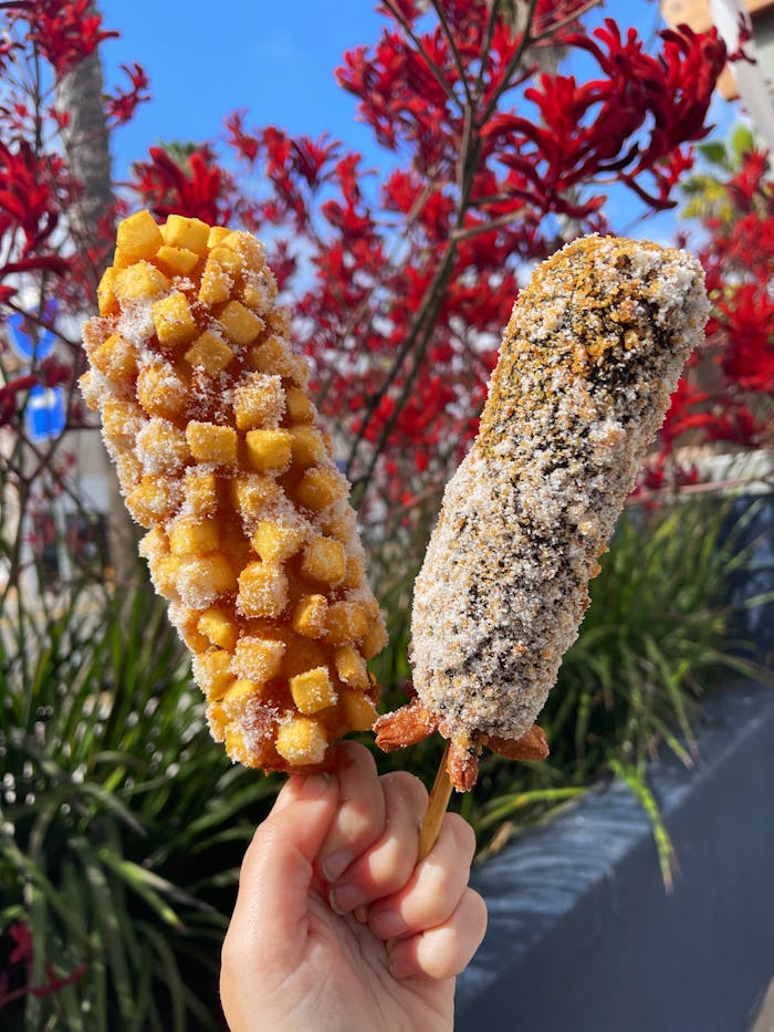 Two corn dogs held outdoors featuring a sugary and savory coating, capturing street food essence.