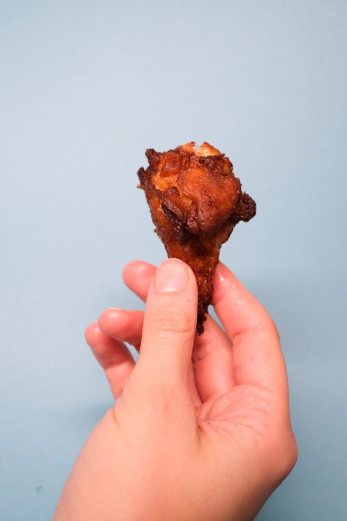 Crop unrecognizable person with fried chicken in arm in bright studio on blue background