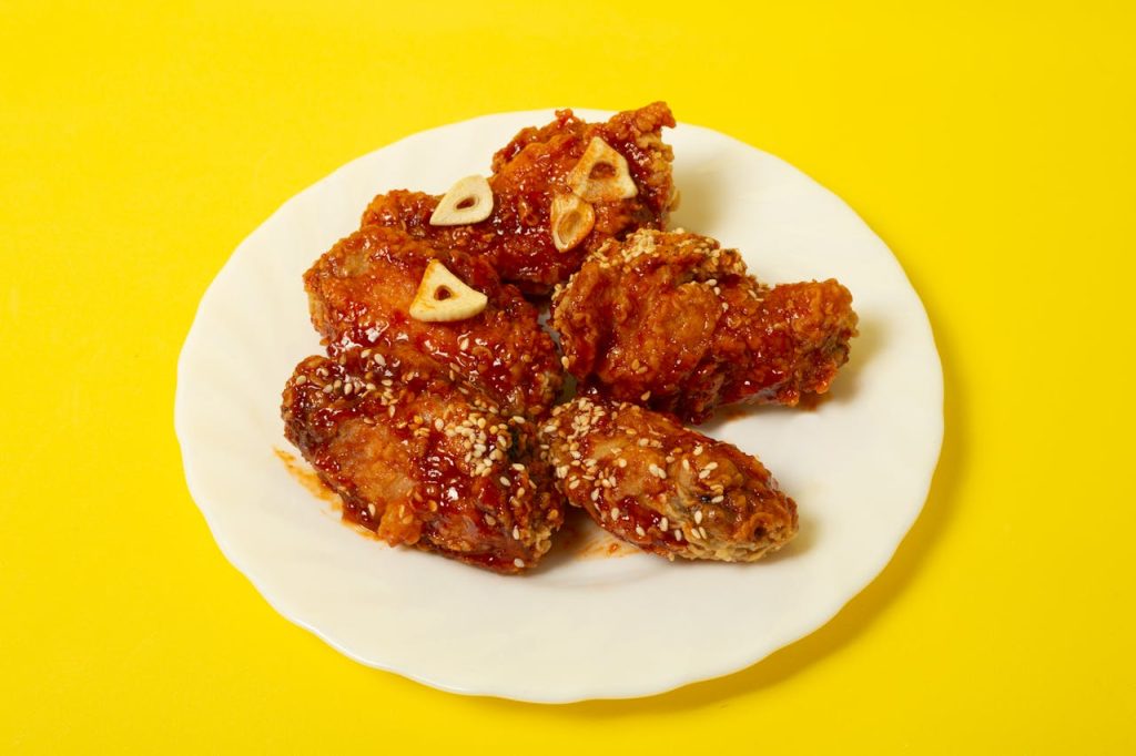 From above of delicious fried chicken meat with sauce and garlic served on white plate on yellow surface in studio