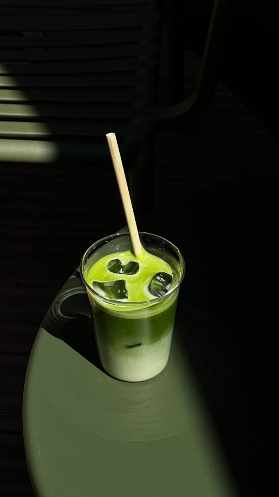 Close-up of a vibrant iced matcha latte on a sunny table, with artistic shadows and a bamboo straw.