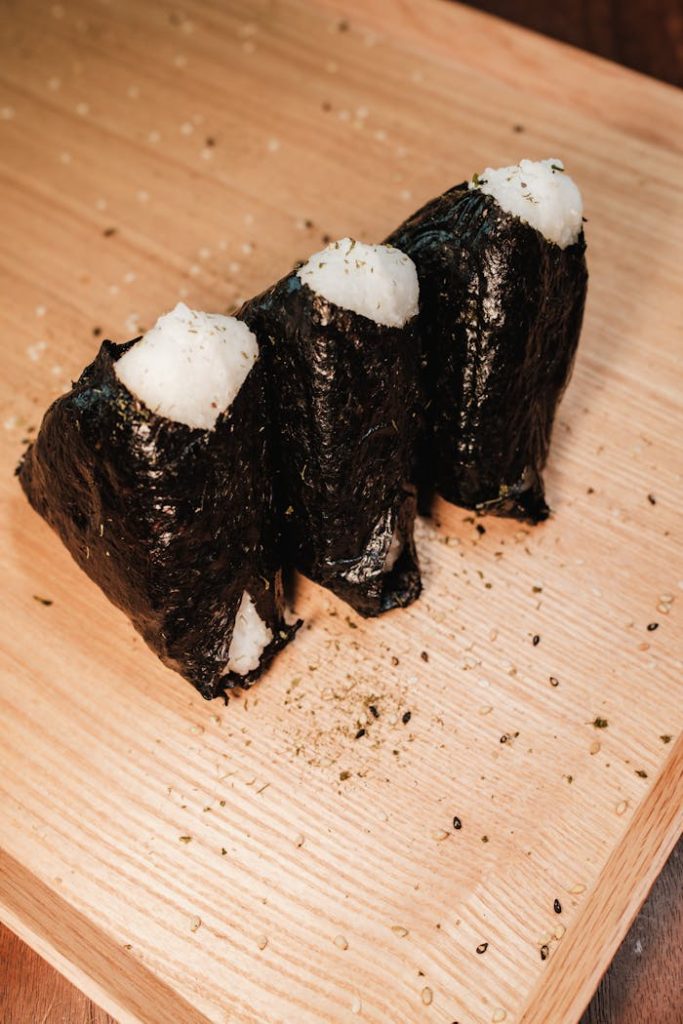 Three delicious Japanese onigiri rice balls wrapped in seaweed on a wooden board.