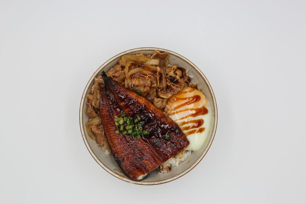A savory unagi donburi bowl featuring grilled eel, rice, and a poached egg with sauce.